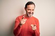 © Krakenimages.com - Middle age hoary man wearing casual orange sweater standing over isolated white background pointing fingers to camera with happy and funny face. Good energy and vibes.