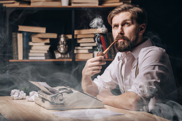 Pensive male author in white shirt with sleeves rolled up smoking pipe and thinking