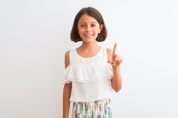 Sticker - Young beautiful child girl wearing casual dress standing over isolated white background showing and pointing up with finger number one while smiling confident and happy.