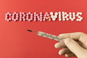 Coronavirus. A human hand with a thermometer on a red background. The inscription coronavirus pills. The concept of virus protection. Selective focus.