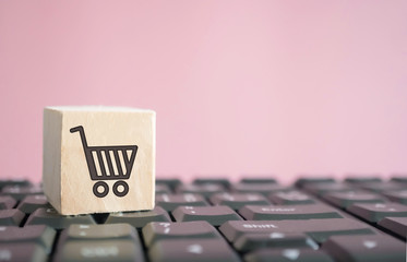 Closed up shopping cart icon on wood cube on computer keyboard. Online shoping business technology.