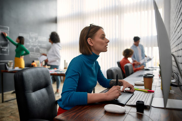 Wall Mural - graphic designer at work. side view of young woman using digital graphics tablet while sitting at he