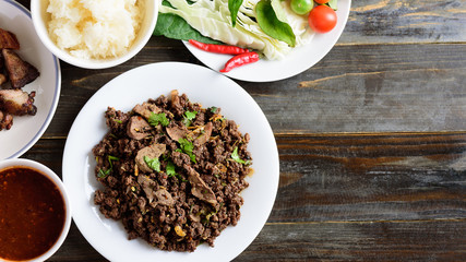 Northern Thai food, spicy minced pork salad (Larb Moo Kua) eating with sticky rice, grilled intestine and fresh vegetables on wooden background, top view