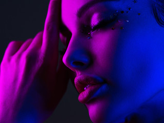 Wall Mural - Portrait of the girl is highlighted in bright blue and purple light. Face of a beautiful model. Colorful portrait of a girl on a dark background. Shiny sequins on the face. Art portrait. Sexy woman.