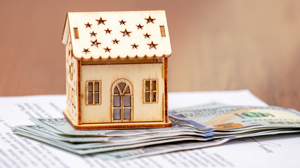 Model of a house near the money and a document on the sale and purchase of housing_