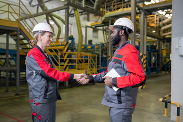 Black foreman with tablet shaking hand of female worker while hiring her at factory