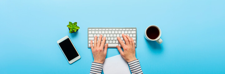 Woman works in the office on a blue background.Only hands Concept workspace, working at a computer, freelance, design. phone, flower, pencil. Banner. Flat lay, top view