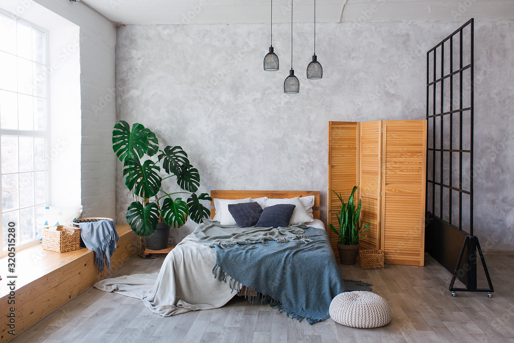 Cozy bedroom area at luxury studio apartment with a free layout in a loft style with big panoramic window and green plant. - obrazy, fototapety, plakaty 
