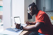 © BullRun - Concentrated young black businessman reading documents and using laptop in office