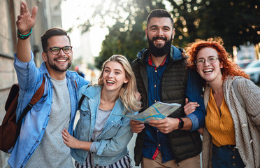 Group of smiling tourists enjoying on vacation, young friends having fun walking on city street during the day.