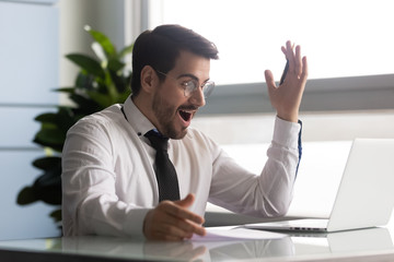 Businessman looks at laptop screen feels amazed got great news