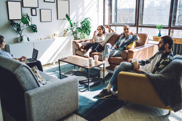 Cheerful friends resting on couch and using laptop at home