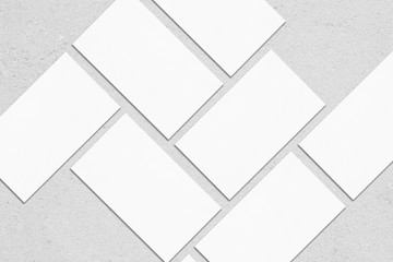 Closeup of empty white rectangle business card mockups lying diagonally on neutral grey concrete background. Flat lay, top view. Open composition. Blank Template for Corporate Identity. Copy space