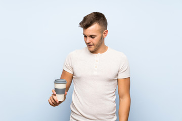 Wall Mural - Young handsome blonde man over isolated blue background holding hot cup of coffee