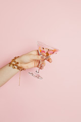 Birthday holiday concept. Female hands showing wine glasses with gold confetti sparkle on pink background