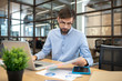 © zinkevych - Bearded man in a blue shirt wearing eyeglasses working in the office and looking involved