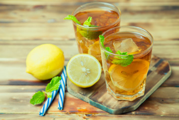 Wall Mural - Iced tea with lemon slices and mint on wood background