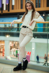 Wall Mural - Portrait of a young beautiful woman in beige sweater and pants posing in the mall