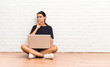 © luismolinero - Young woman with a laptop sitting on the floor doing silence gesture