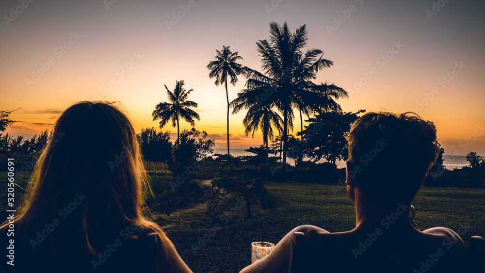 a young couple watching the sunset with palm trees in Tanzania Africa - obrazy, fototapety, plakaty 