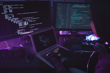 unrecognizable young man surrounded by multiple screens programming or hacking security in dark room