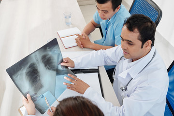 Pulmonologist discussing lungs x-ray of patient with his team and searching for signs of coronovirus disease