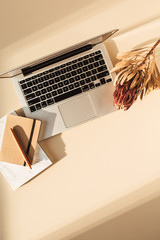 Wall Mural - Home office table desk workspace with laptop, tropical protea flower, notebook on pastel beige background. Flat lay, top view freelance business concept for social media, blog, magazine.