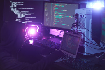 side view at unrecognizable hacker using computer equipment with programming code on screens in dark
