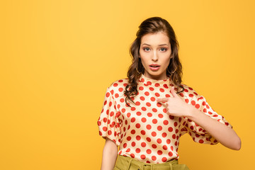 Wall Mural - shocked young woman pointing with finger at herself while looking at camera isolated on yellow