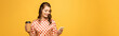 panoramic shot of happy young woman holding coffee to go and using smartphone isolated on yellow