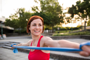 Young woman doing exercise outdoors in city with elastic bands.