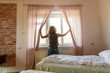 © pikselstock - Rear view of tourist in the hotel room pulling the curtains to see the view