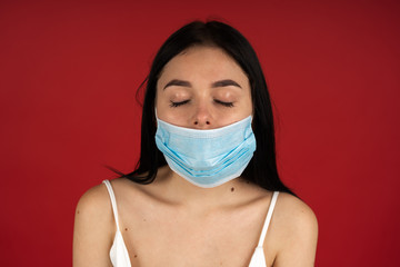 Front view of ill woman in medical mask posing with closed eyes isolated on red background