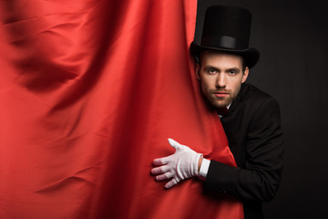 Wall Mural - handsome magician in suit and hat in circus with red curtains