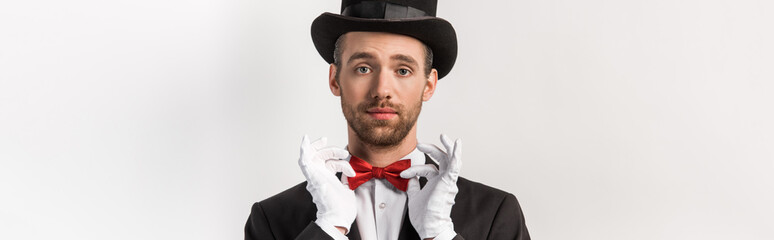 Wall Mural - panoramic shot of confident magician adjusting red bow tie, isolated on grey