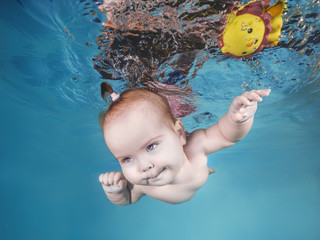 Cute chubby little girl plays with toy underwater in a swimming pool