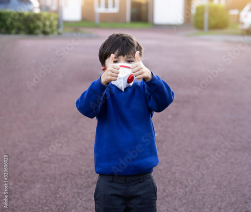 Portrait of of School kid wearing protective face mask for pollution or virus, Child in school uniform wearing protection mask and showing thumbs up while waiting for school bus in the morning.