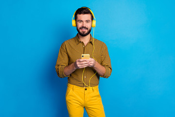 Sticker - Portrait of positive cheerful guy listen music radio songs he search internet on cellphone wear shine total yellow headset checkered pants isolated over blue color background