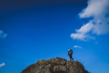 Hiker woman on the rock cliff against the clearly blue sky and cloud