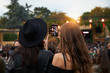 © Indico Studio/ADDICTIVE STOCK - Back view of stylish girl friends in black hat taking selfie and watching photo on mobile phone in bright day at festival