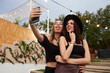 © Indico Studio/ADDICTIVE STOCK - Stylish cheerful girl friends in black hat embracing and taking selfie on mobile phone in bright day at decorated arena on festival
