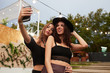 © Indico Studio/ADDICTIVE STOCK - Stylish cheerful girl friends in black hat embracing and taking selfie on mobile phone in bright day at decorated arena on festival