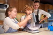 © PHILIPPE DEGROOTE/ADDICTIVE STOCK - Stock photo of a girl pouring liquid sugar into a bowl with a boy and a woman next door in a kitchen