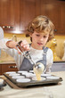 © PHILIPPE DEGROOTE/ADDICTIVE STOCK - Vertical stock photo of a child with an apron emptying cream on plates ready to make cupcakes