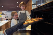 © PHILIPPE DEGROOTE/ADDICTIVE STOCK - Stock photo of two boys watching as a girl with a glove pulls a silver from the oven full of muffins