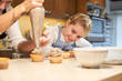 © PHILIPPE DEGROOTE/ADDICTIVE STOCK - Stock photo of a blonde girl with apron watching as a girl puts cream on top of a cupcake with a pastry sleeve with two children on the side watching