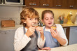 © PHILIPPE DEGROOTE/ADDICTIVE STOCK - Stock photo of two kids with apron eating cupcakes in the kitchen