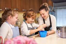 Stock Photo Of A Boy With Apron Breaking An Egg In The Kitchen With A Blonde Girl And A Girl Next Door Preparing Cupcakes