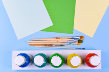 A set of acrylic paints in jars for the artist. Different color paints and brushes on a blue background. Flat lay. Copy space