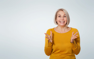 Wall Mural - middle aged blonde emotionally posing in a studio. happy woman in yellow bright sweater on white bac
